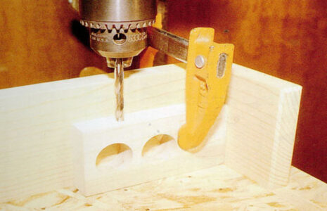 clamp holding a board with holes in it under a drill